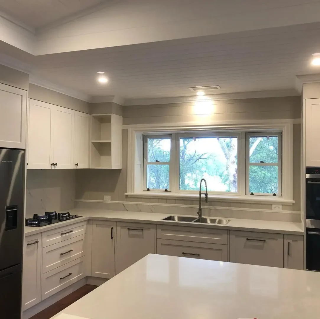 Modern kitchen with white cabinets and large window.