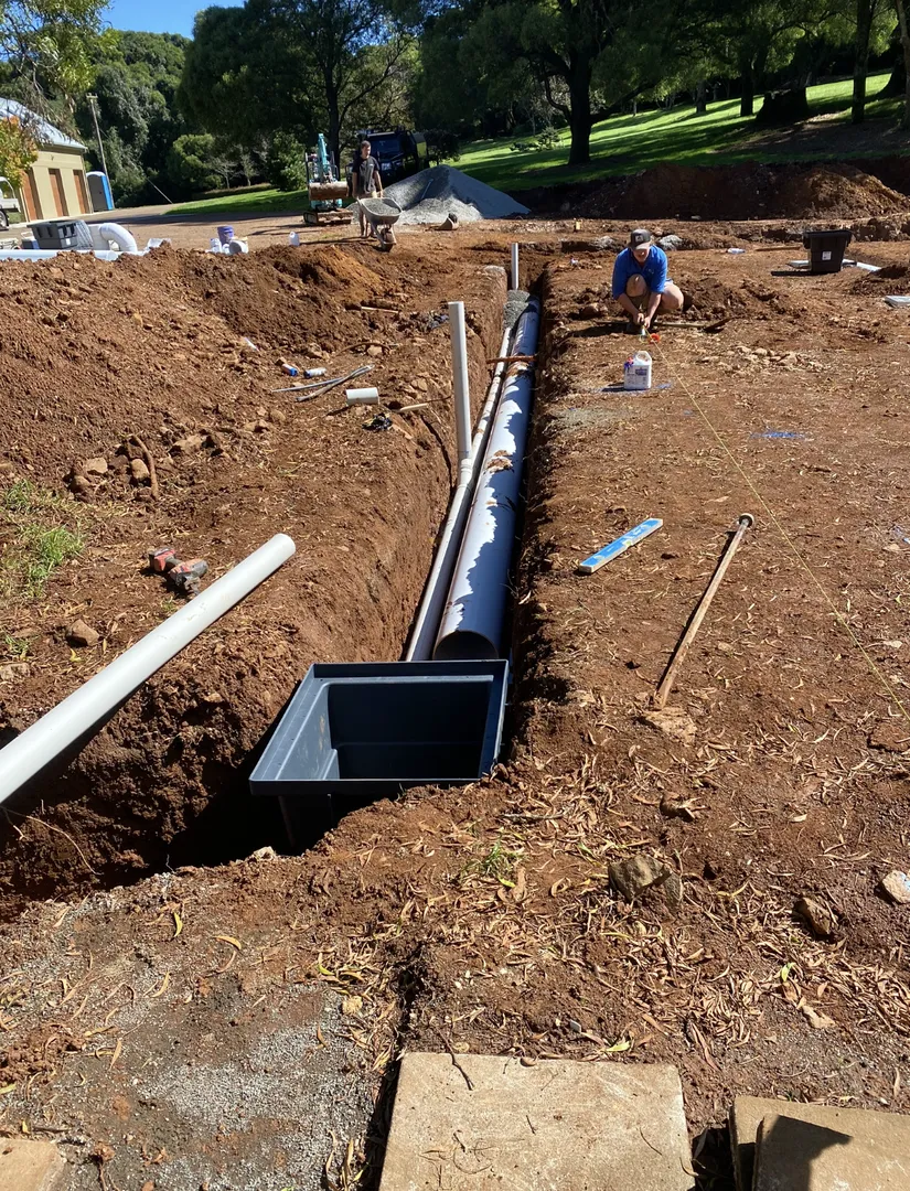 Workers installing drainage pipes in a trench.