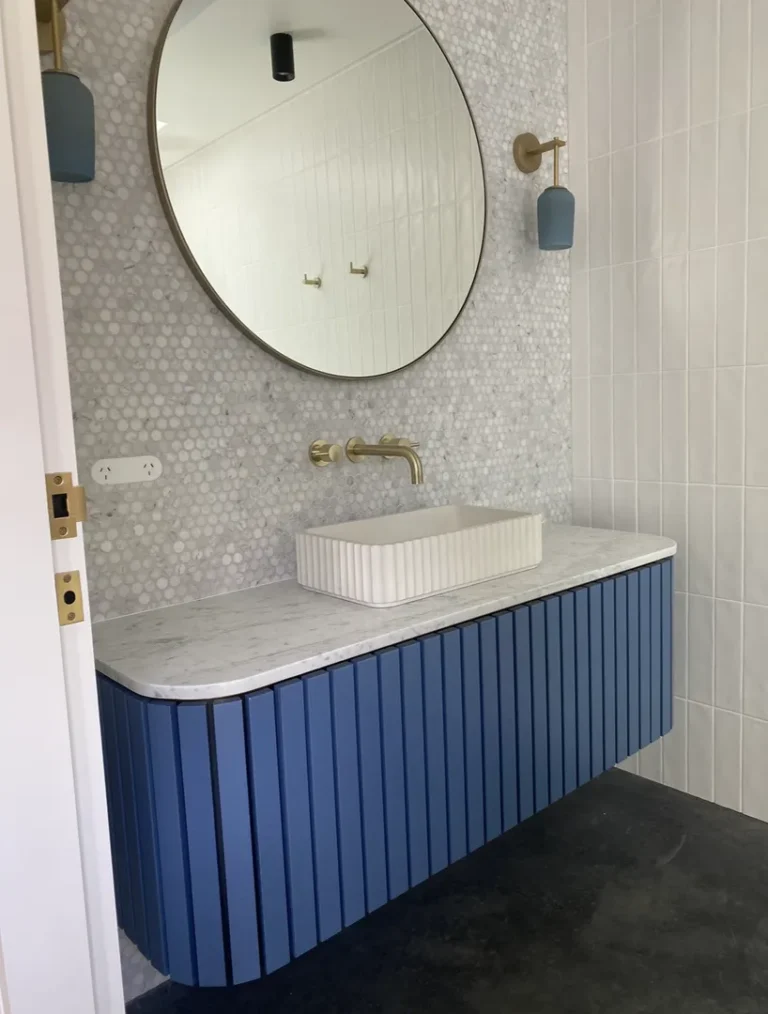 Modern bathroom with circular mirror and blue cabinet.